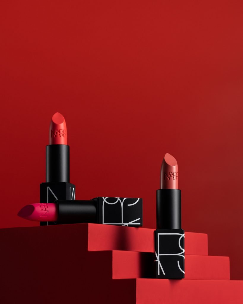 Creative photography of the Lipstick positioned on the red platform with three steps. The background is red